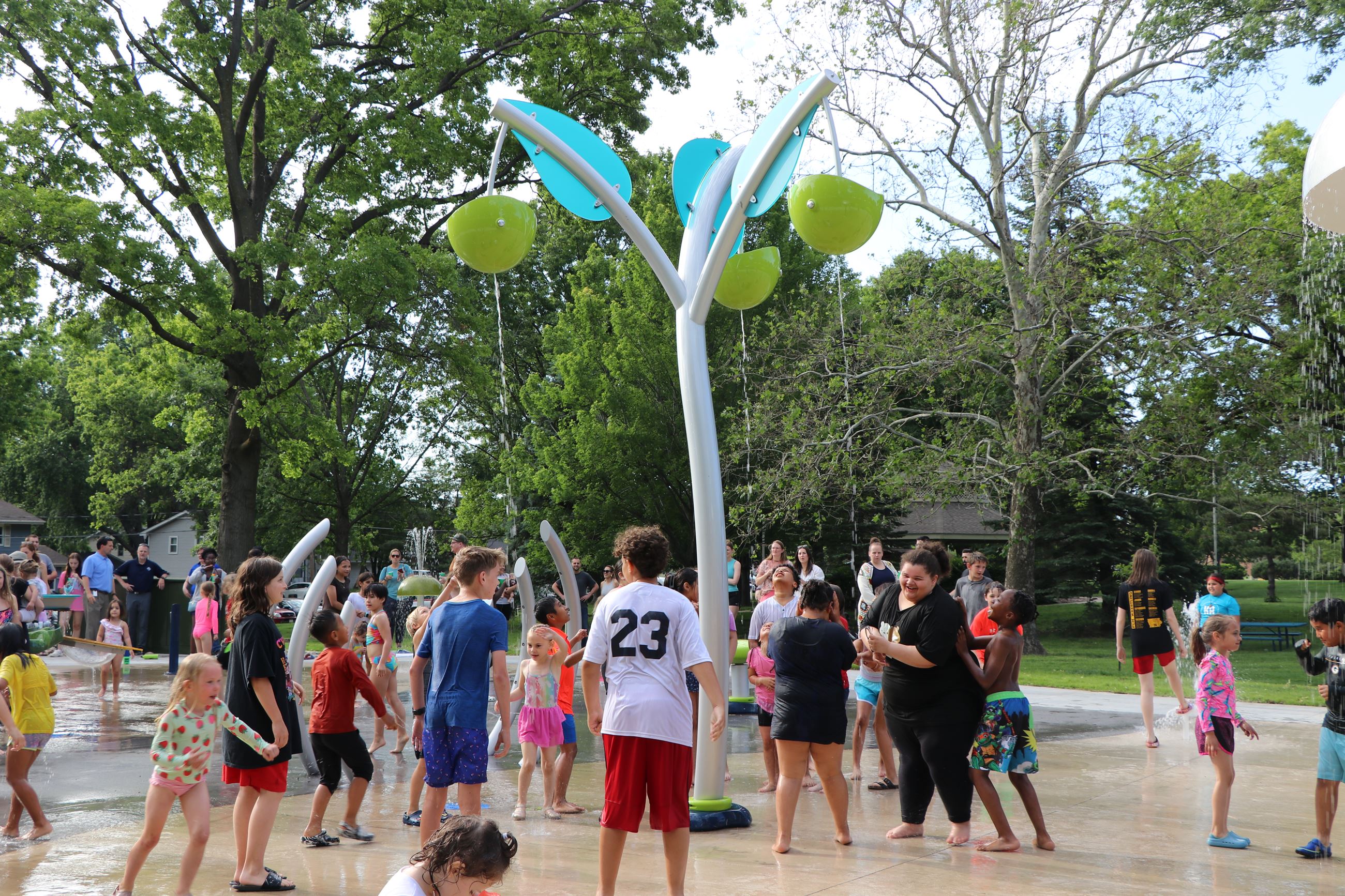 Kids gathering around the splash pad as water falls on them.