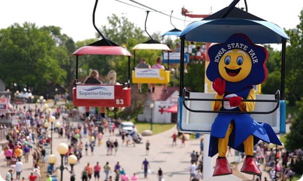 Iowa State Fair blue ribbon mascot waving while sitting on the skyglider at the Iowa State Fair